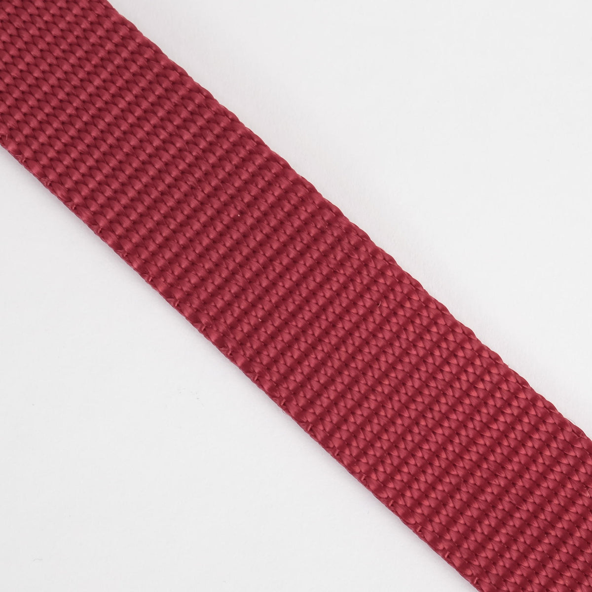 A close-up of a textured red woven strap or ribbon diagonally placed on a plain white background.