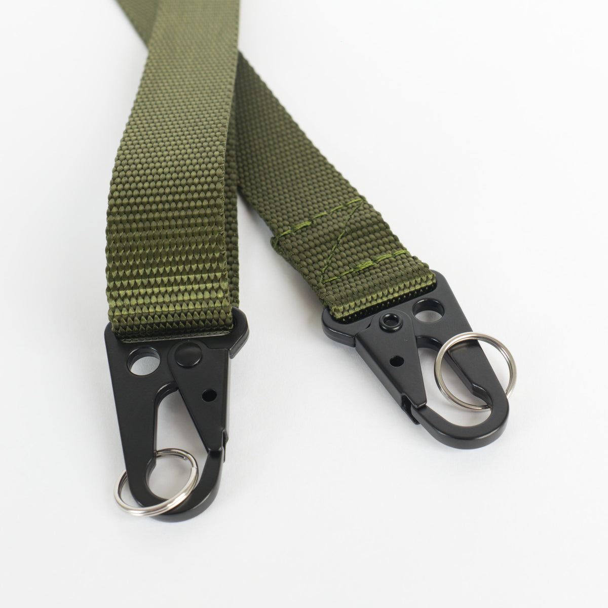 An olive nylon adjustable strap with black metal clips and black plastic slider close up image of the HK clips on a white background.