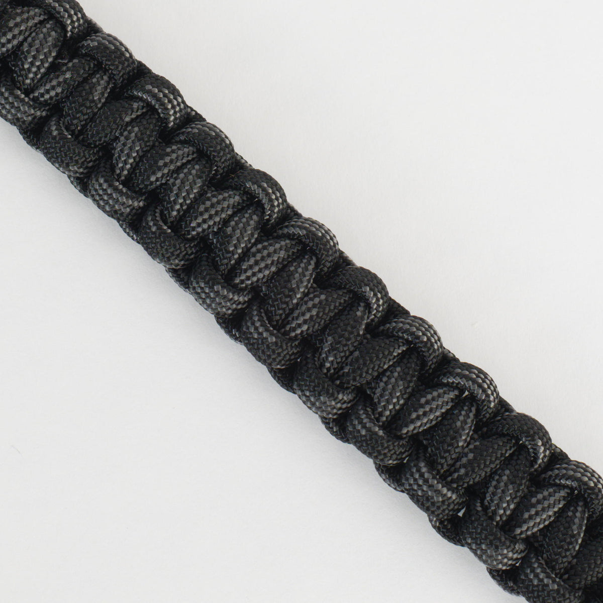 A close-up of a black paracord bracelet or strap with a woven, braided texture, shown diagonally on a plain white background.