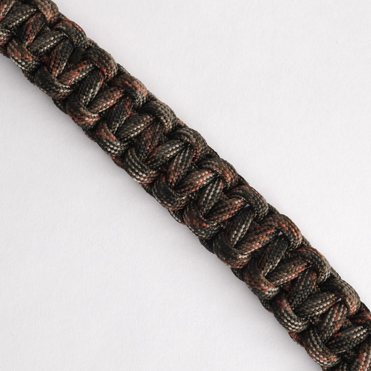 A close-up of a woven paracord bracelet or strap made from black, gray, and rust-orange threads, shown diagonally on a plain white background.