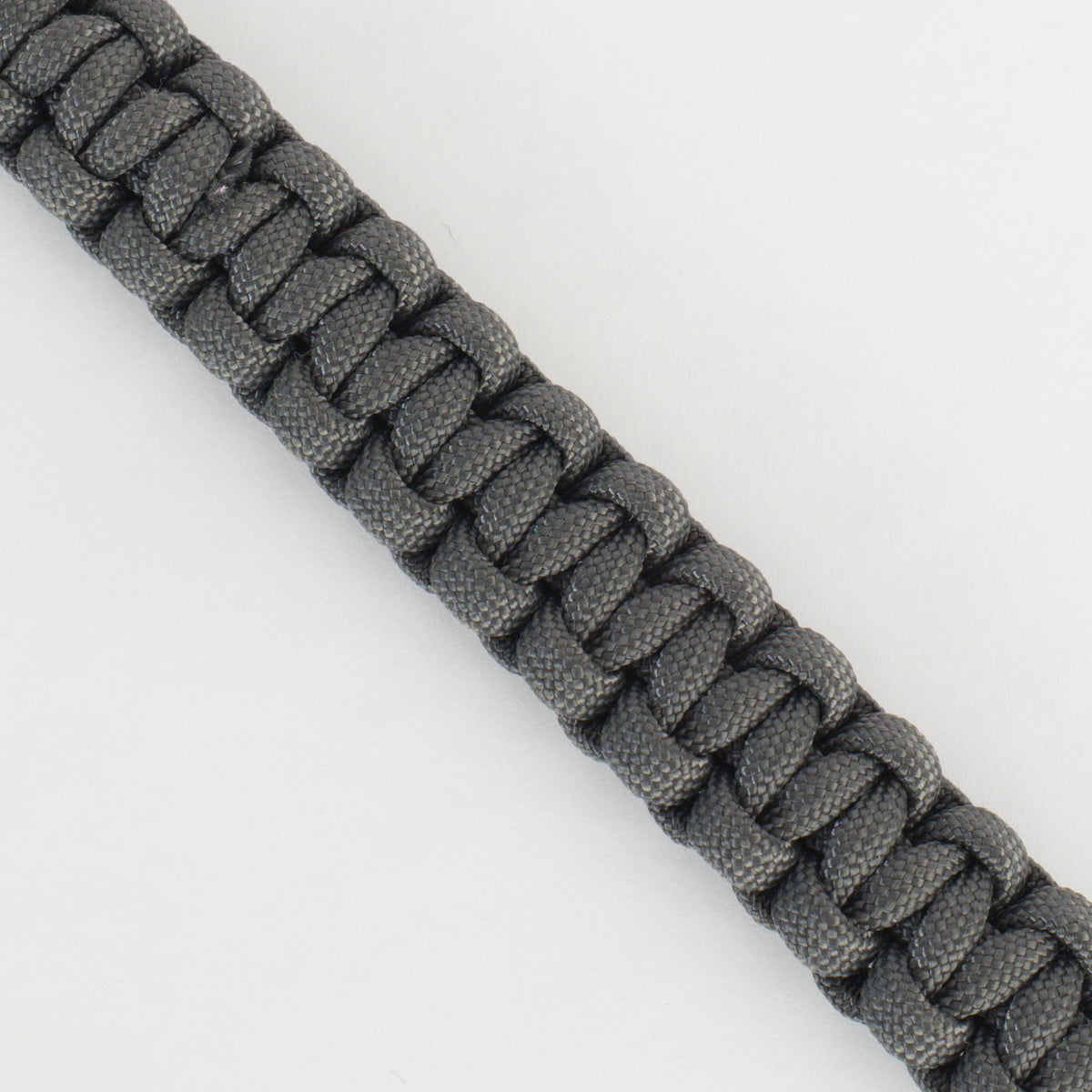 A close-up of a dark gray paracord bracelet or strap with a braided woven texture, shown diagonally on a plain white background.