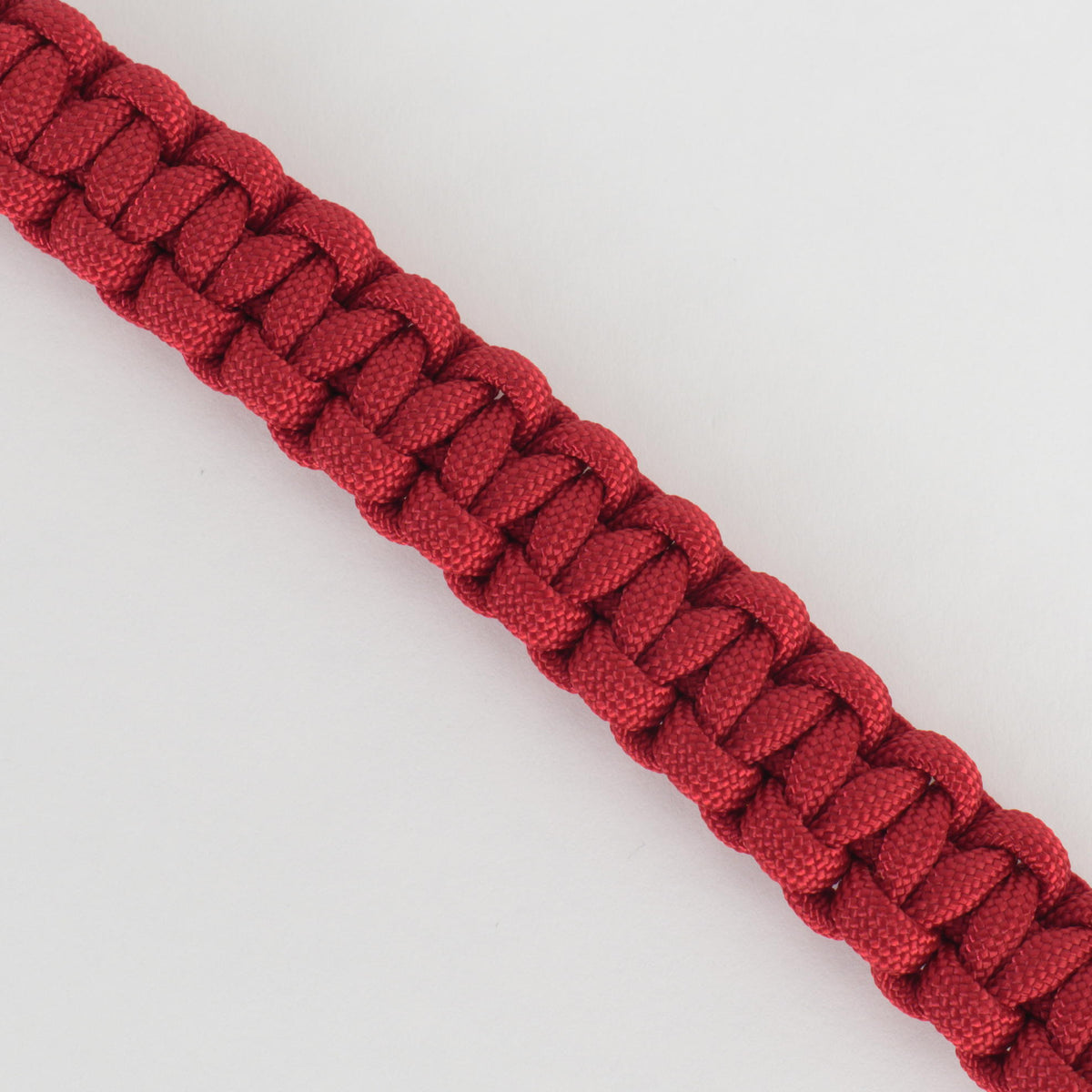 A close-up of a red paracord bracelet or strap with a woven basketweave pattern, shown diagonally on a plain white background.
