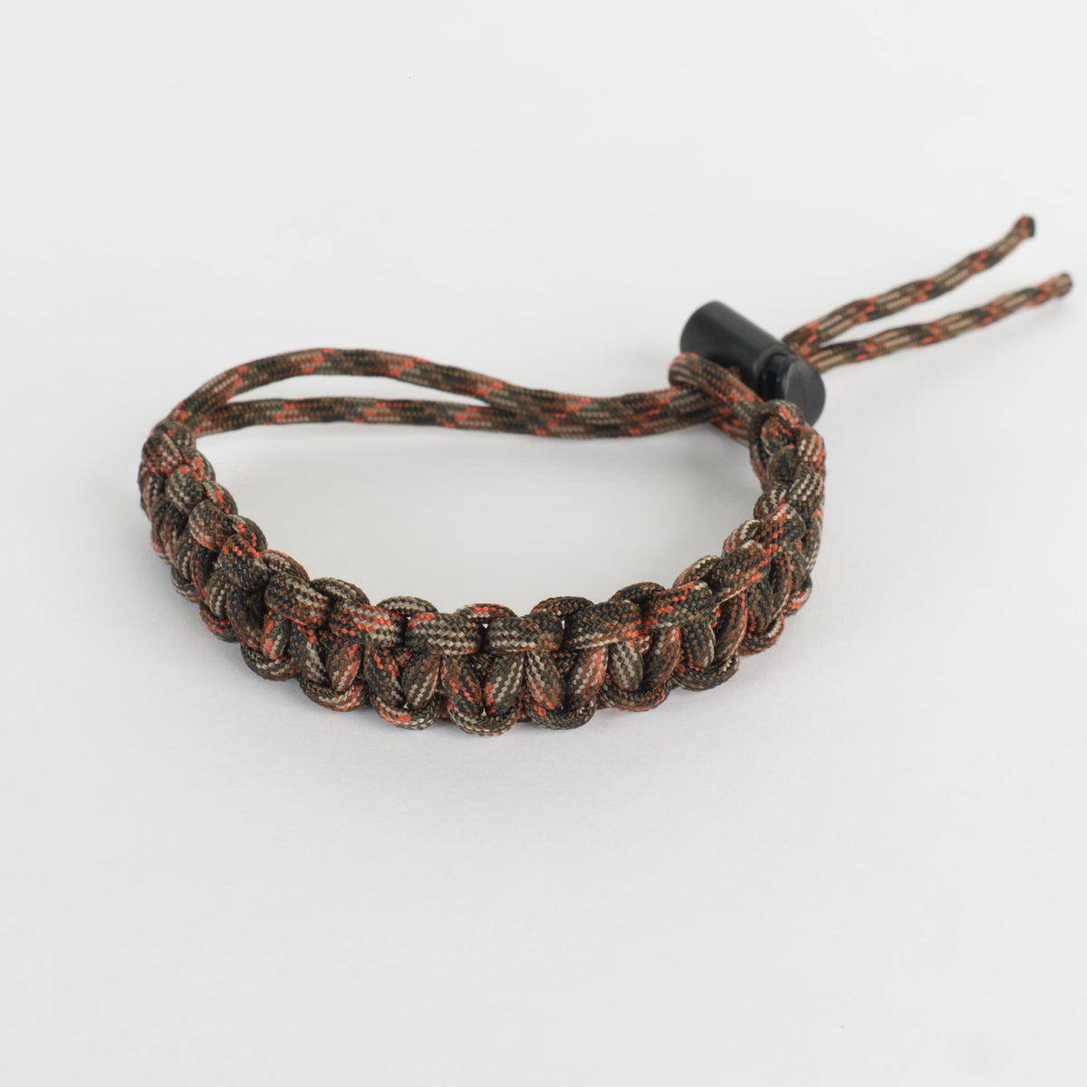 A paracord bracelet with a camouflage pattern of brown, black, and orange, featuring a black plastic toggle clasp, shown on a light gray background.
