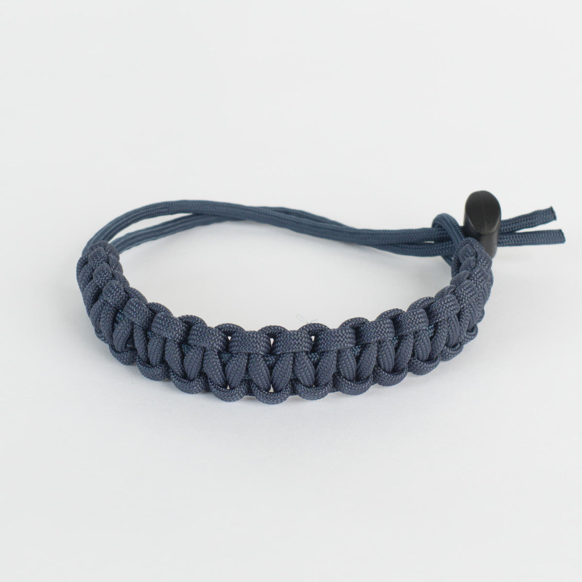 A dark slate blue paracord bracelet with a woven pattern and a black plastic toggle clasp, shown on a clean white background.