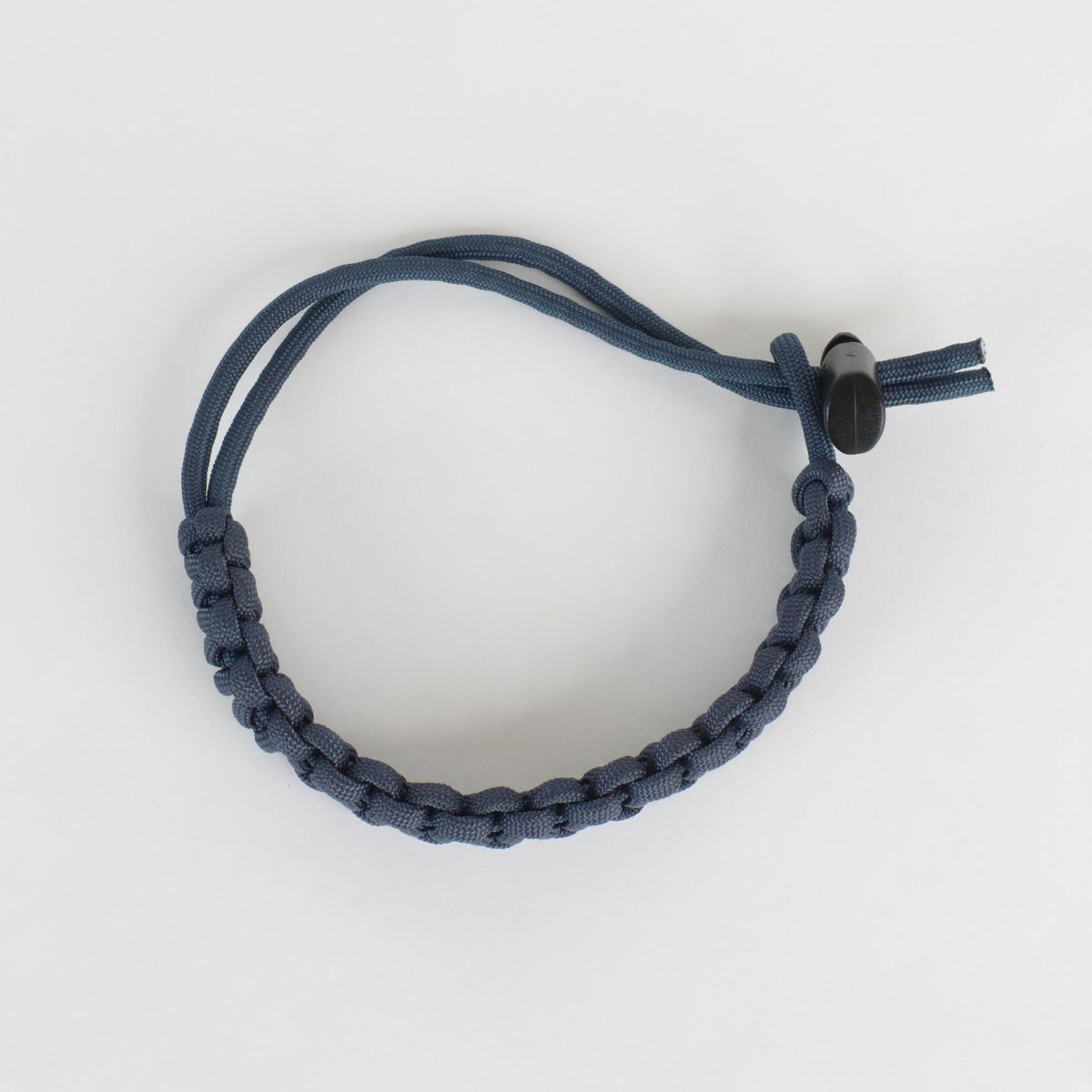 A dark blue paracord bracelet with a black plastic toggle clasp, photographed on a clean white background.