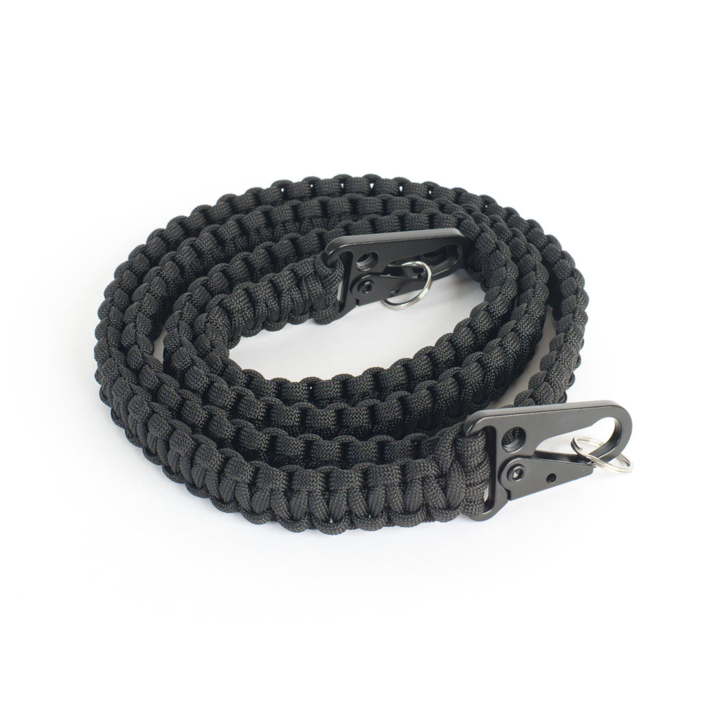 A coiled black paracord sling strap with black metal snap hooks shown on a plain white background.