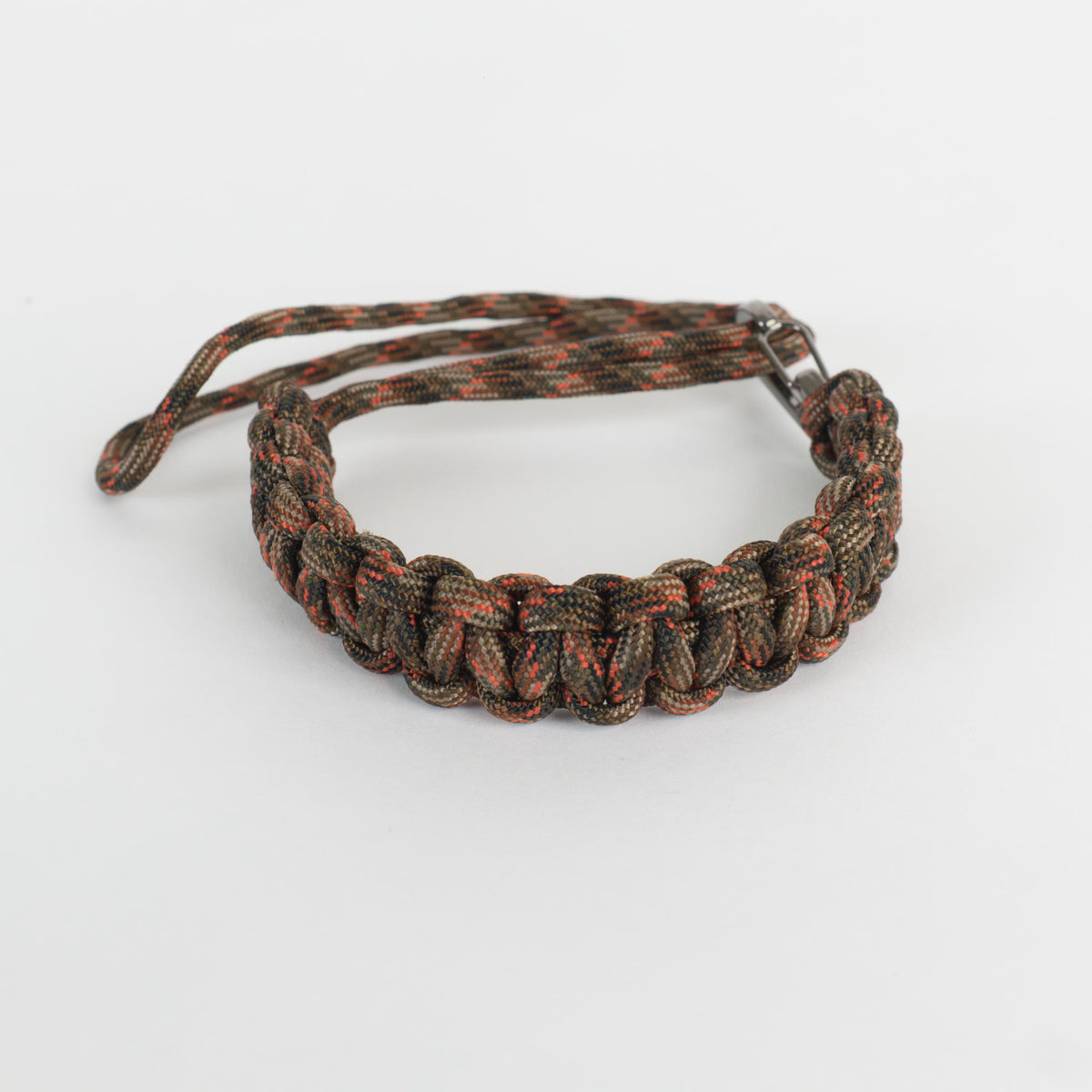 A woven paracord bracelet in a camouflage pattern of brown, black, and orange, featuring a metal clasp, shown on a plain white background.