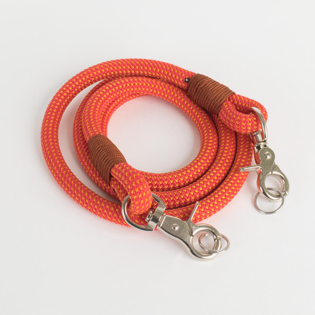 An orange rope strap with brown wrapped sections and silver metal snap hooks, displayed on a clean white background.